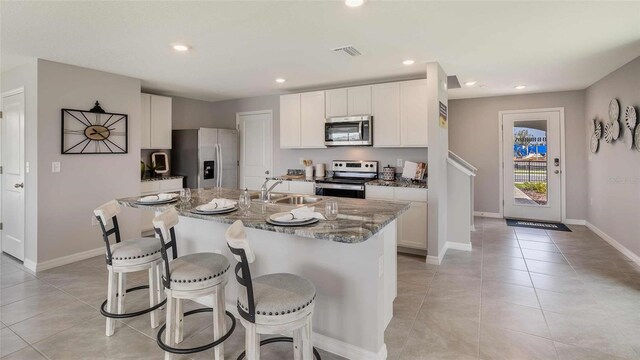 kitchen with dark stone countertops, stainless steel appliances, sink, a center island with sink, and a breakfast bar