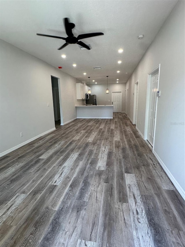 unfurnished living room featuring ceiling fan and dark wood-type flooring