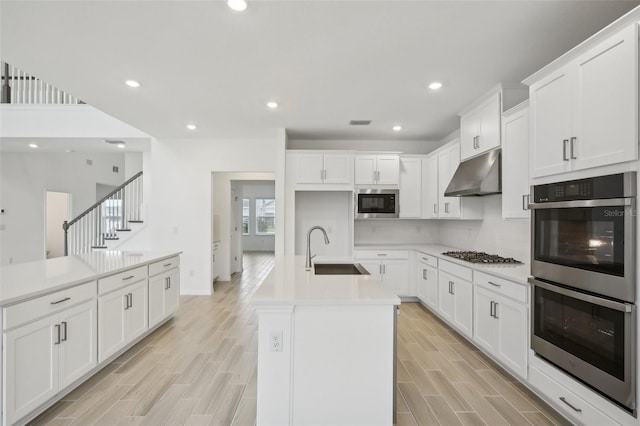 kitchen featuring appliances with stainless steel finishes, light wood-type flooring, sink, white cabinetry, and an island with sink