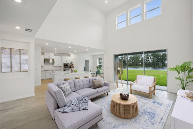 living room with light hardwood / wood-style flooring, a healthy amount of sunlight, and a high ceiling