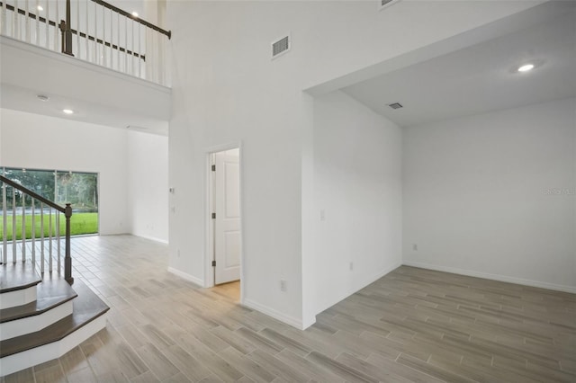 empty room with light wood-type flooring and a towering ceiling