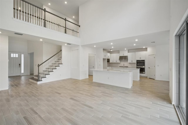 unfurnished living room featuring light hardwood / wood-style floors, a towering ceiling, and a healthy amount of sunlight