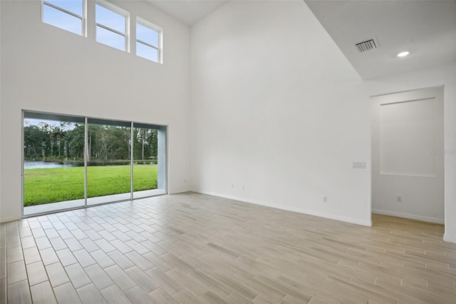 empty room with a healthy amount of sunlight, light wood-type flooring, and a high ceiling