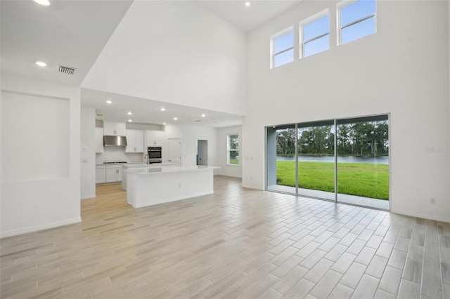 unfurnished living room featuring a high ceiling, light hardwood / wood-style floors, and sink