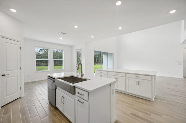 kitchen with a kitchen island with sink, light hardwood / wood-style flooring, white cabinets, and stainless steel dishwasher