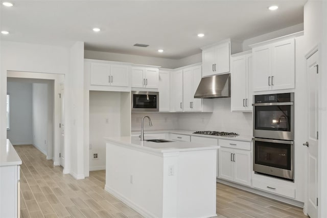 kitchen featuring white cabinetry, sink, range hood, a center island with sink, and appliances with stainless steel finishes