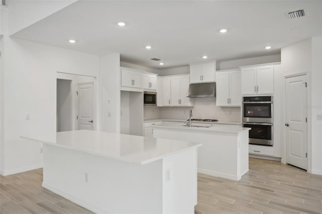 kitchen featuring white cabinetry, an island with sink, light wood-type flooring, and appliances with stainless steel finishes