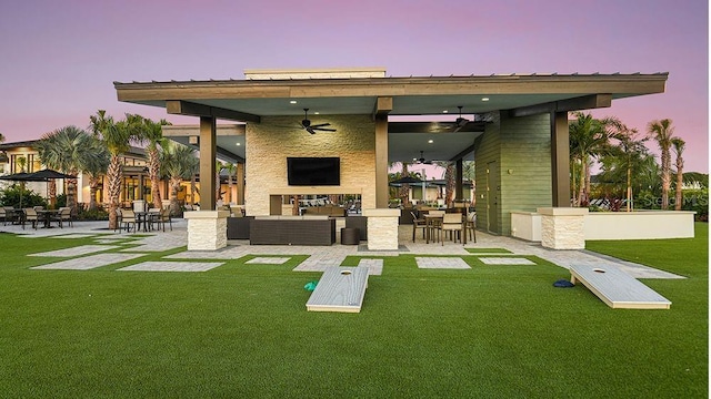 back house at dusk with an outdoor living space, ceiling fan, a patio area, and a lawn