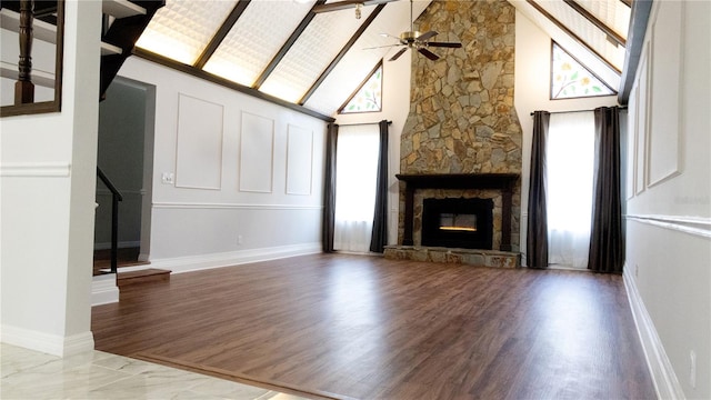 unfurnished living room featuring high vaulted ceiling, light wood-type flooring, a healthy amount of sunlight, and a stone fireplace