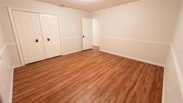 unfurnished bedroom with hardwood / wood-style floors, crown molding, a closet, and a textured ceiling