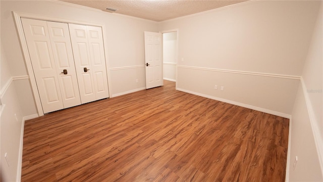 unfurnished bedroom with ornamental molding, a textured ceiling, a closet, and wood-type flooring