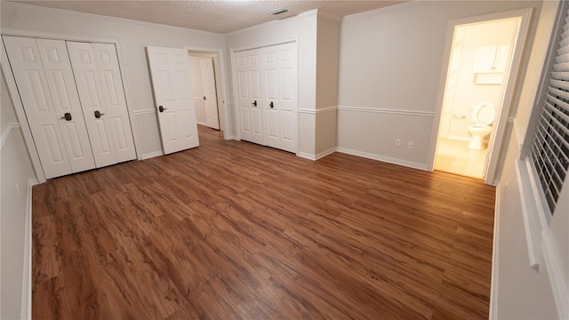 unfurnished bedroom featuring crown molding, dark wood-type flooring, a textured ceiling, and ensuite bathroom