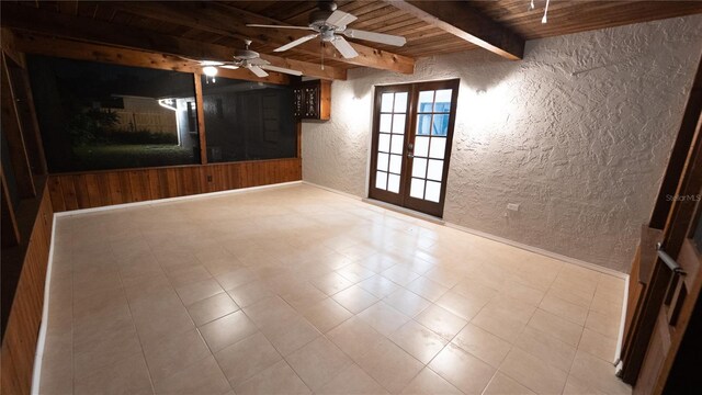 tiled empty room featuring ceiling fan, wooden ceiling, beamed ceiling, and french doors