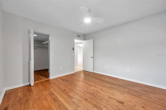 unfurnished bedroom featuring ceiling fan, a spacious closet, light wood-type flooring, and a closet