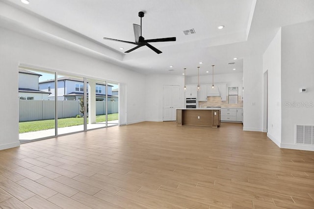 unfurnished living room with light hardwood / wood-style flooring, ceiling fan, and a raised ceiling