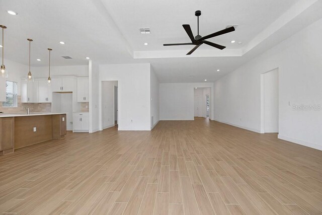 unfurnished living room with a tray ceiling and light wood-type flooring