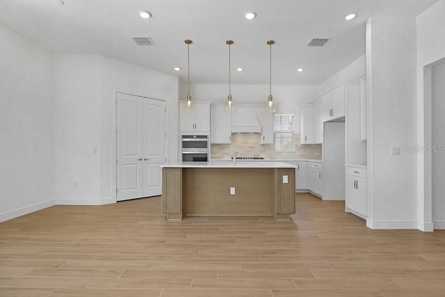 kitchen featuring white cabinets, a center island with sink, visible vents, and light countertops