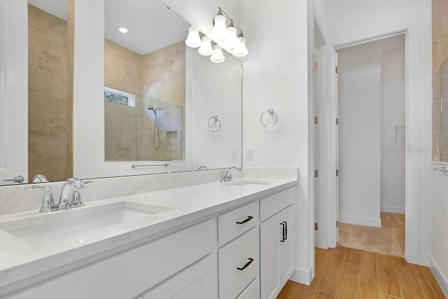 bathroom with double vanity, a walk in shower, a sink, and wood finished floors