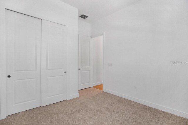 unfurnished bedroom featuring light carpet, visible vents, baseboards, and a closet