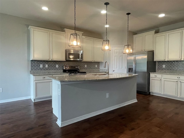 kitchen with appliances with stainless steel finishes, hanging light fixtures, an island with sink, light stone counters, and sink