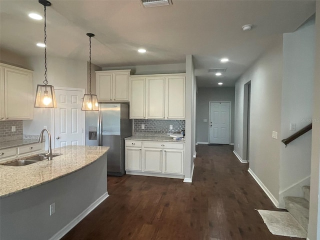 kitchen with decorative light fixtures, light stone countertops, stainless steel fridge, sink, and dark wood-type flooring