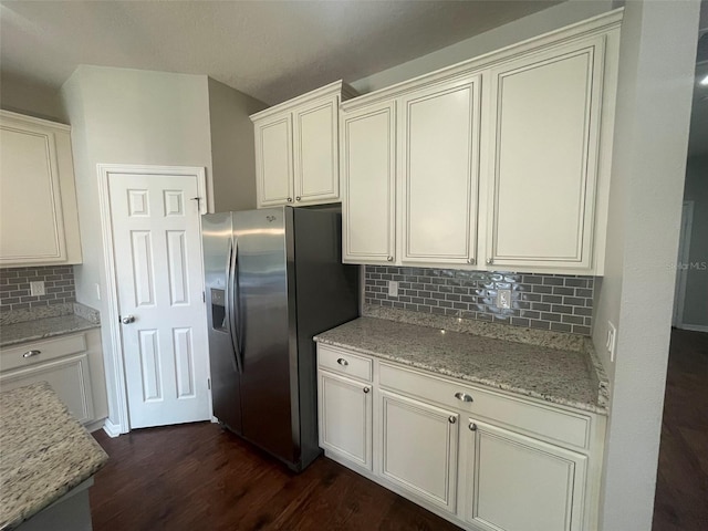 kitchen with dark wood-type flooring, light stone countertops, stainless steel fridge, and decorative backsplash