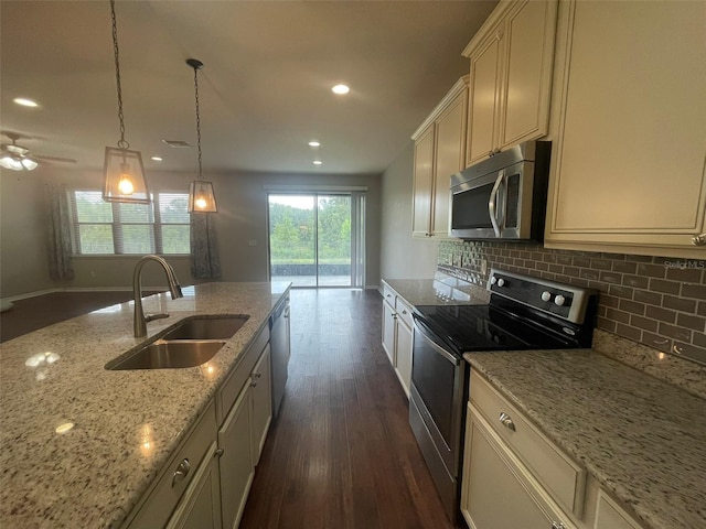 kitchen featuring stainless steel appliances, cream cabinetry, light stone countertops, sink, and pendant lighting