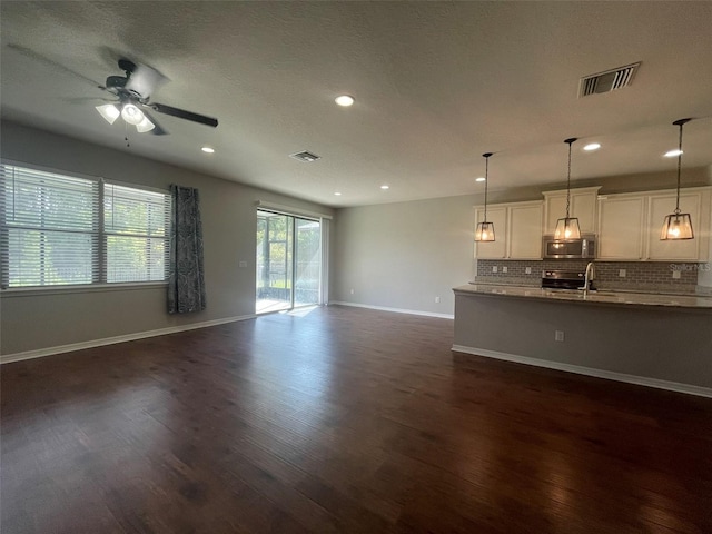 unfurnished living room featuring dark hardwood / wood-style flooring, ceiling fan, sink, and a textured ceiling