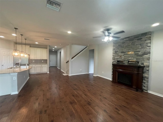 unfurnished living room with ceiling fan, sink, a stone fireplace, and dark wood-type flooring