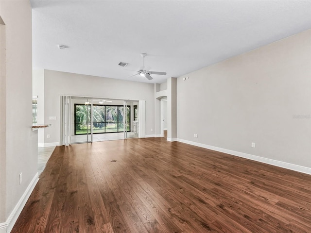 unfurnished living room with baseboards, ceiling fan, arched walkways, and dark wood-style flooring