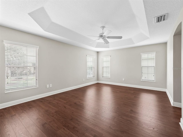 spare room featuring baseboards, visible vents, a raised ceiling, ceiling fan, and dark wood-type flooring