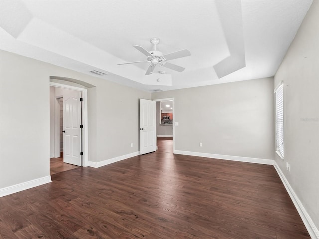 spare room featuring baseboards, visible vents, a raised ceiling, and dark wood-type flooring