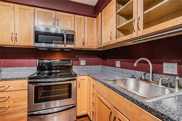 kitchen featuring light brown cabinetry, a sink, glass insert cabinets, appliances with stainless steel finishes, and dark countertops