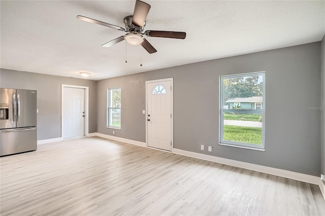 unfurnished living room featuring ceiling fan, light wood-type flooring, and a textured ceiling