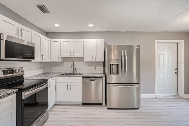 kitchen with sink, appliances with stainless steel finishes, light hardwood / wood-style floors, light stone counters, and white cabinetry