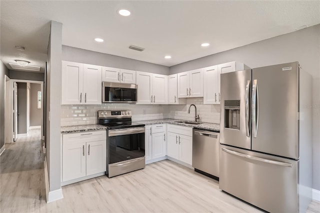 kitchen with sink, decorative backsplash, appliances with stainless steel finishes, light stone counters, and white cabinetry