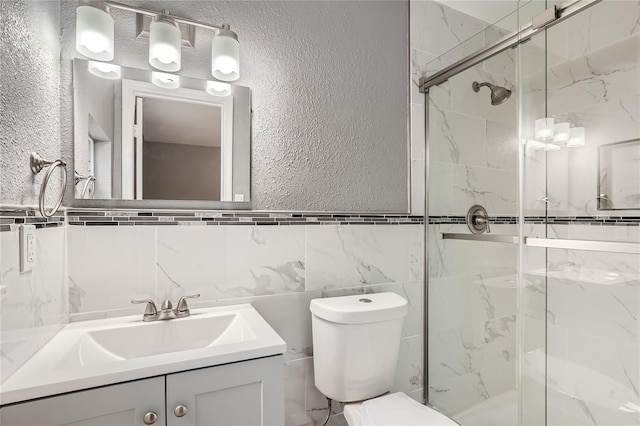 bathroom with a shower with door, vanity, tile walls, and toilet