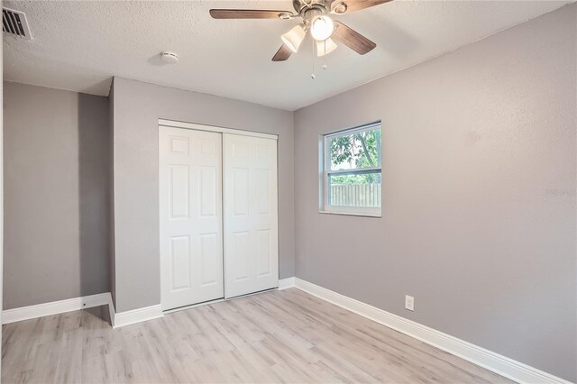 unfurnished bedroom with ceiling fan, a closet, a textured ceiling, and light hardwood / wood-style flooring