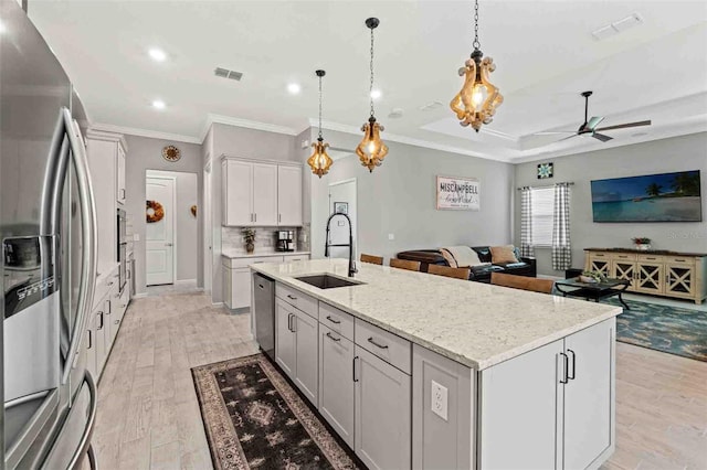 kitchen featuring sink, an island with sink, decorative light fixtures, appliances with stainless steel finishes, and light wood-type flooring