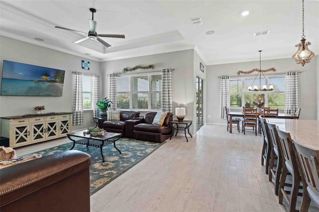 living room with ceiling fan with notable chandelier, ornamental molding, a raised ceiling, and light wood-type flooring