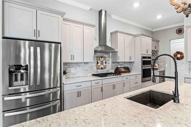 kitchen featuring wall chimney range hood, light stone countertops, sink, and appliances with stainless steel finishes