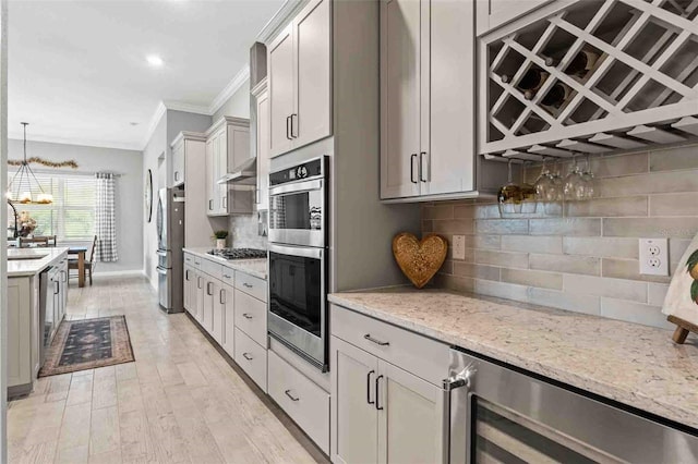 kitchen featuring light stone counters, ornamental molding, appliances with stainless steel finishes, pendant lighting, and beverage cooler