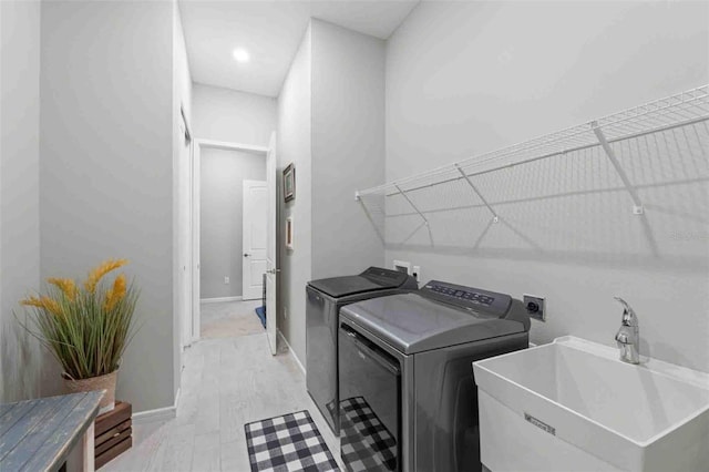 clothes washing area featuring sink, light hardwood / wood-style floors, and washer and dryer