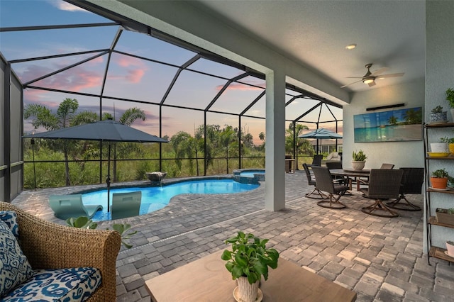 pool at dusk with a lanai, a patio area, ceiling fan, and an in ground hot tub