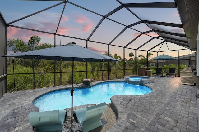 pool at dusk with a patio area, an in ground hot tub, and glass enclosure