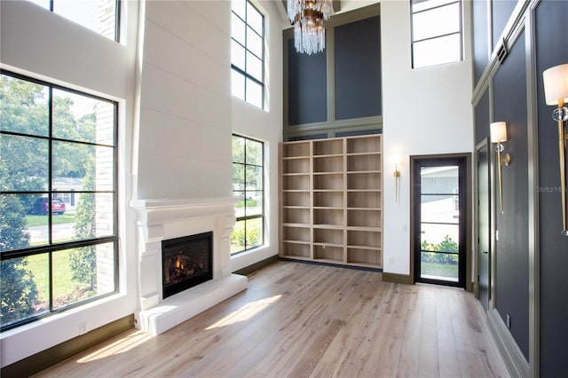 unfurnished living room featuring a warm lit fireplace, a notable chandelier, a high ceiling, wood finished floors, and baseboards