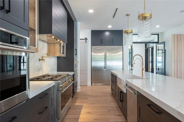 kitchen featuring light wood finished floors, a barn door, high quality appliances, light stone countertops, and a sink