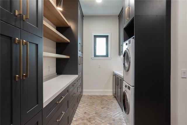 washroom featuring cabinet space, baseboards, brick floor, and stacked washer and clothes dryer