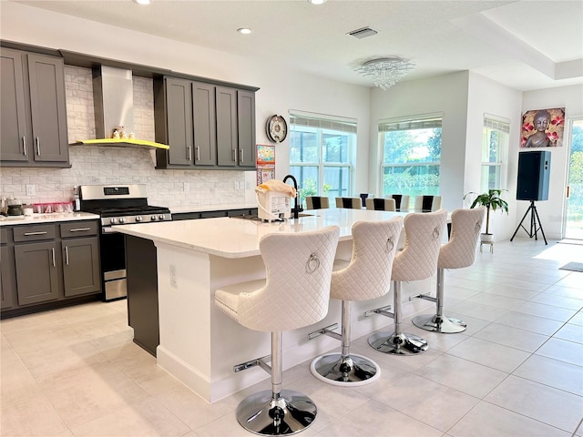 kitchen with a breakfast bar, light countertops, visible vents, stainless steel range with gas stovetop, and wall chimney exhaust hood