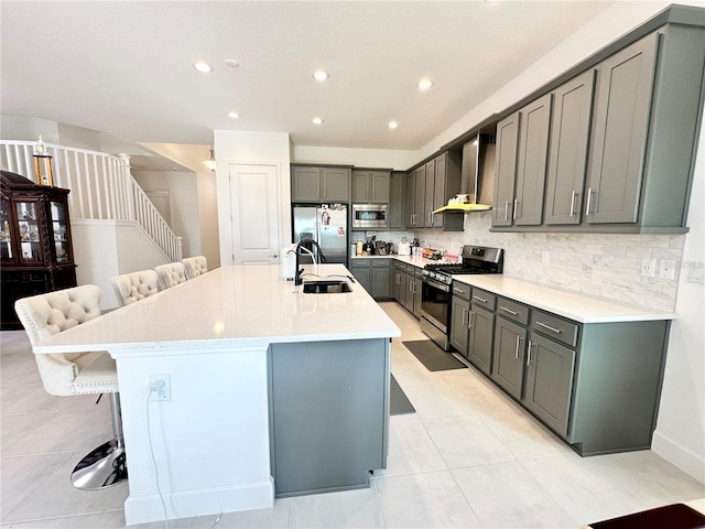 kitchen with wall chimney exhaust hood, stainless steel appliances, gray cabinetry, a kitchen bar, and a sink